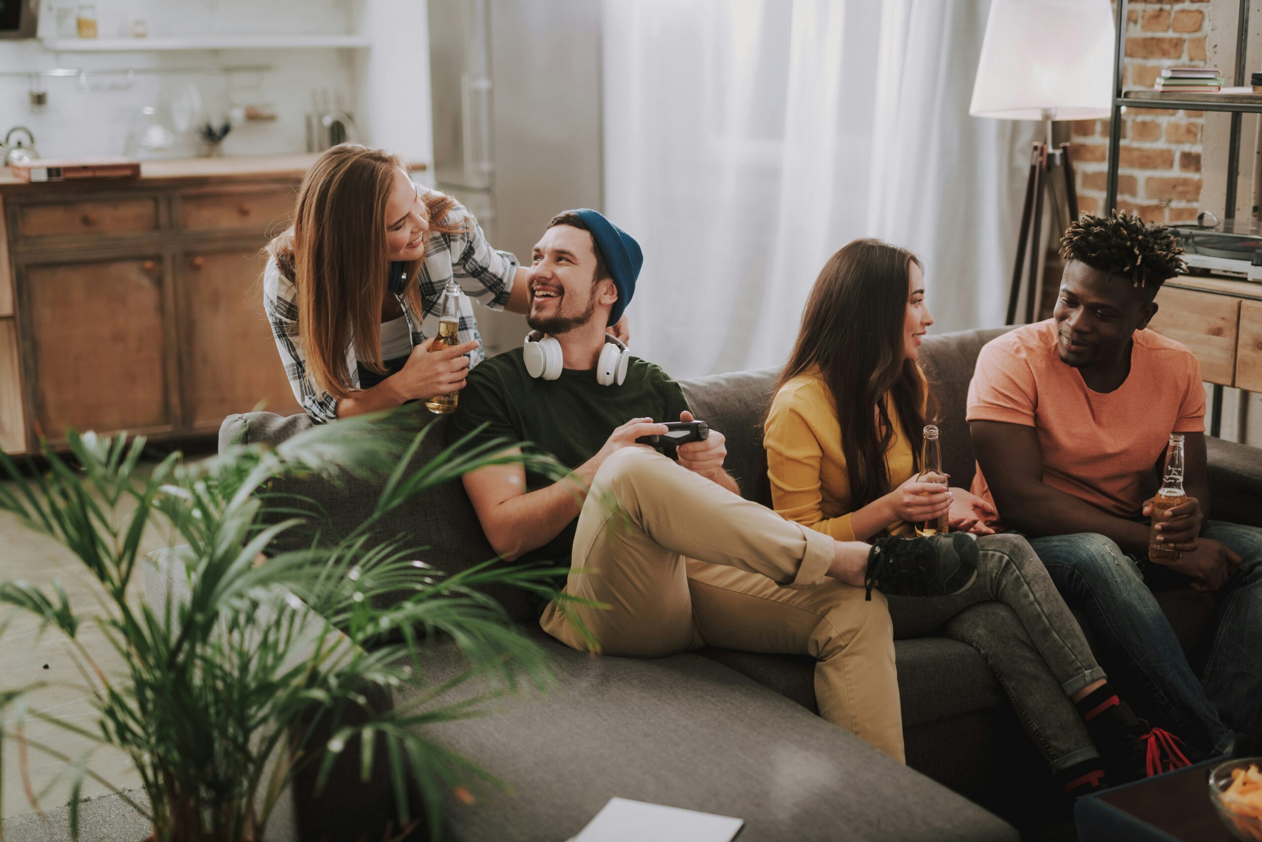 Sterling Tiger Valley Four friends sitting on a couch, chatting, laughing, and holding drinks in a cozy living room.
