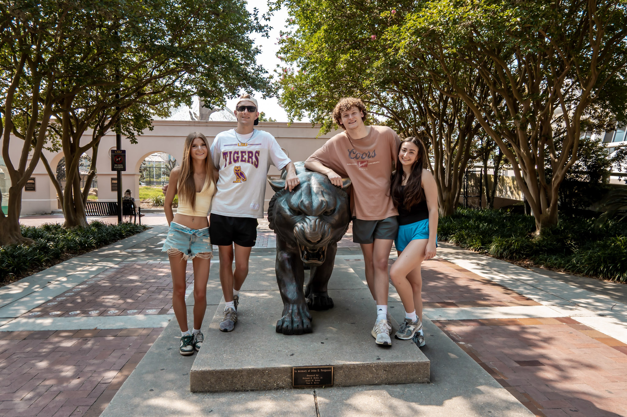 Sterling Tiger Valley Four people pose by a tiger statue on a tree-lined campus walkway under a sunny sky.