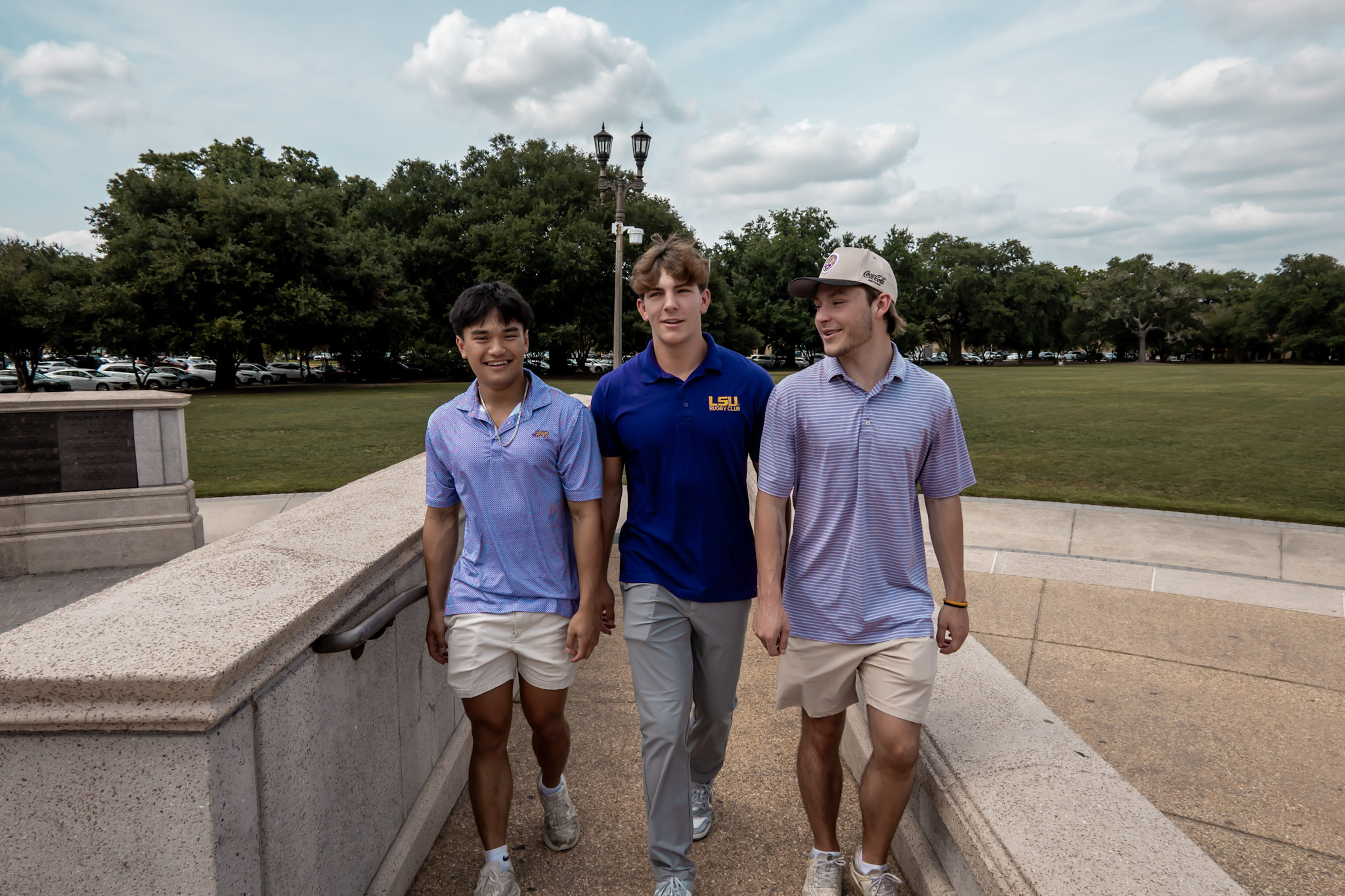 Sterling Tiger Valley Three young men walk outdoors on a sunny day, wearing casual shirts and shorts, with trees in the background.