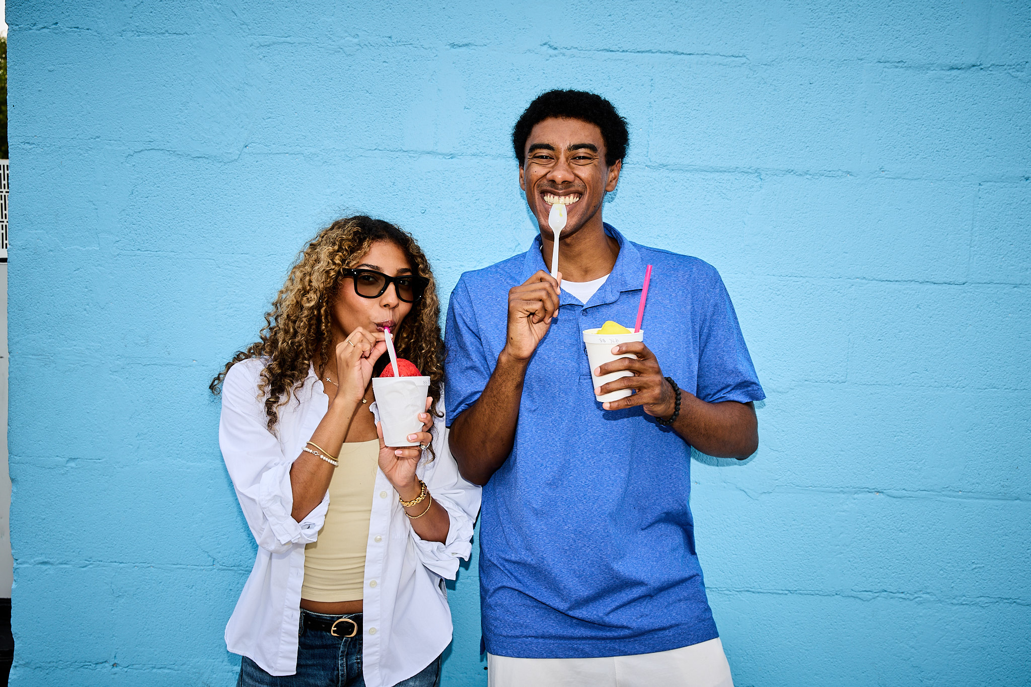 Sterling Tiger Valley Two people smiling and eating frozen treats in front of a bright blue wall, enjoying a casual moment together.
