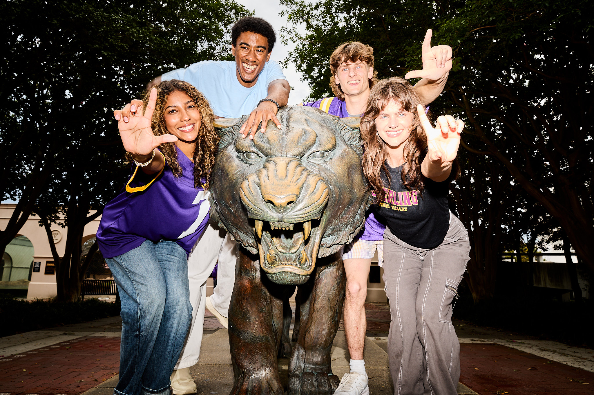Sterling Tiger Valley Four smiling students pose with a tiger statue outdoors, all making an L gesture with their hands.