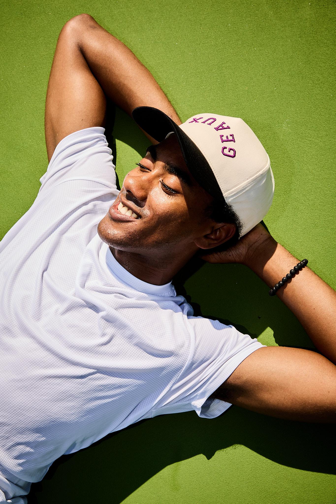 Sterling Tiger Valley Smiling man in white shirt and cap lies on bright green surface with hands behind his head, eyes closed.