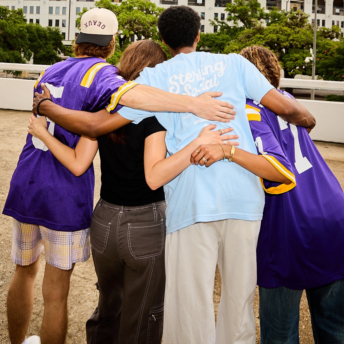 Sterling Tiger Valley Four people stand close together outdoors, arms around each other, facing away from the camera, showing camaraderie and friendship.