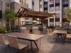 Sterling Tiger Valley Modern outdoor patio with tables, woven chairs, a pergola, grills, greenery, and apartment buildings in the background.