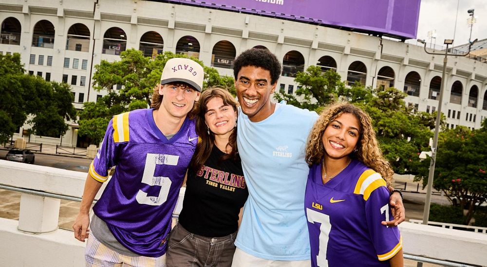 Sterling Tiger Valley Four smiling people stand together in front of Tiger Stadium at LSU, wearing LSU jerseys and casual clothes.