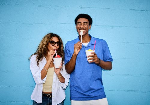Sterling Tiger Valley Two people smiling and eating frozen treats in front of a bright blue wall, enjoying a casual moment together.