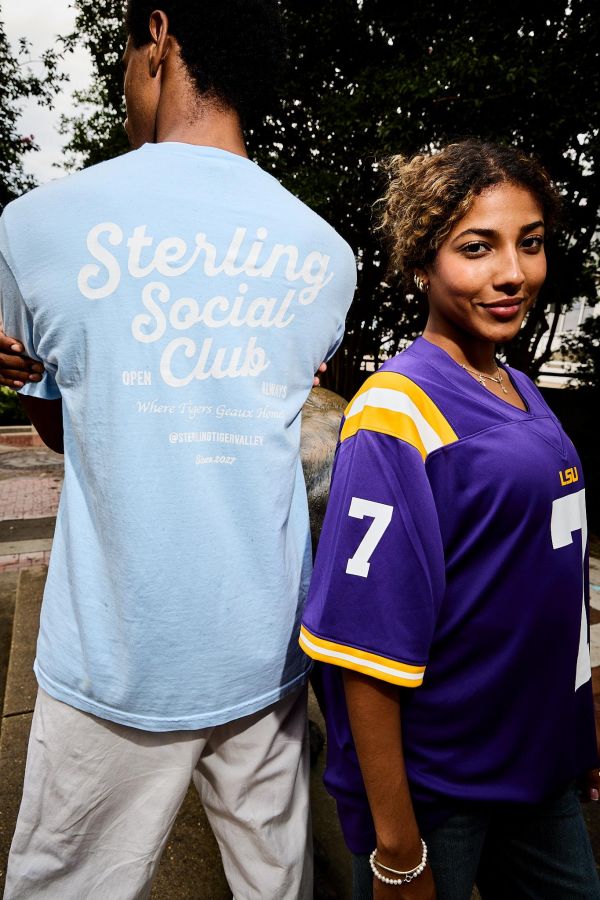 Sterling Tiger Valley Two people stand back-to-back; one wears a light blue shirt, the other wears a purple LSU jersey with the number 7.