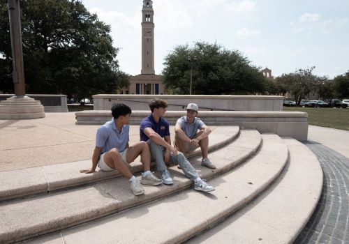 Sterling Tiger Valley Three young men sit and talk on outdoor steps near a tall clock tower and trees on a sunny day.